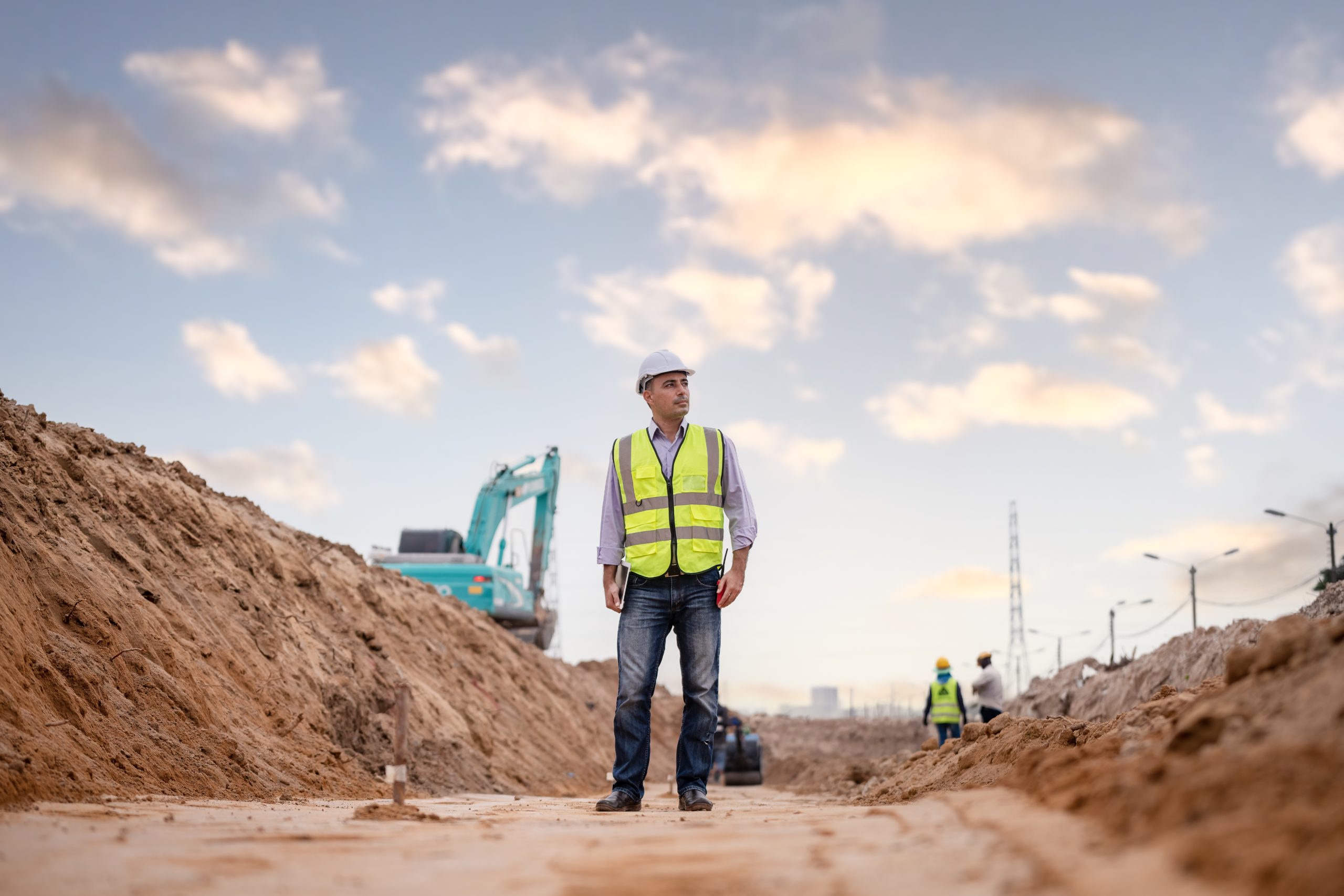 Construction engineer wearing safety vest and hard hat at noisy excavation site